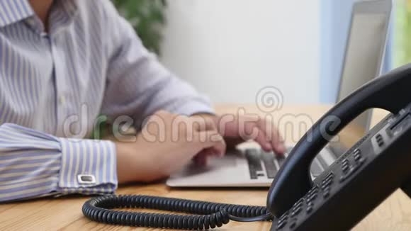 在工作区的桌面键盘上商人的手焦点是座机电话背景模糊关门视频的预览图