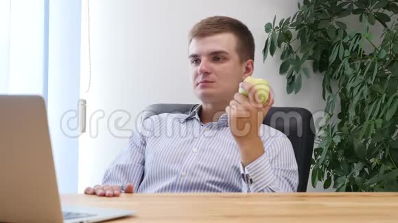 年轻的商人正在办公室里吃苹果同时他正在看手提电脑快关门复制空间4K视频的预览图
