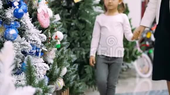 年轻的母亲和小女儿正在商店里挑选一棵圣诞树视频的预览图