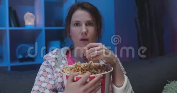一张美国女人拿着爆米花坐在沙发上看着恐怖的东西吃着爆米花和视频的预览图