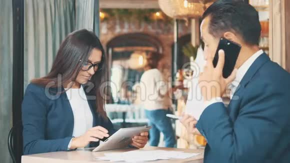 两个穿深蓝色西装的商人正在工作女人在用平板电脑坐在咖啡店里有人在说话视频的预览图