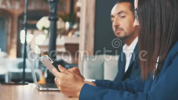两位身着深蓝色西装的商人正坐在咖啡厅里开发笔记本电脑和平板电脑侧视图庄稼关闭视频的预览图