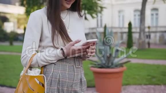 在漂亮的房子附近用智能手机吸引了一位带着米色帽子长发的微笑年轻女子视频的预览图