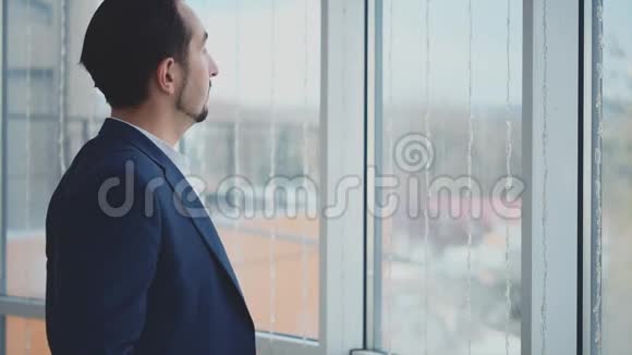正式套房的商人站在全景窗口前可以看到城市景色严肃的男人交叉双臂概况视频的预览图