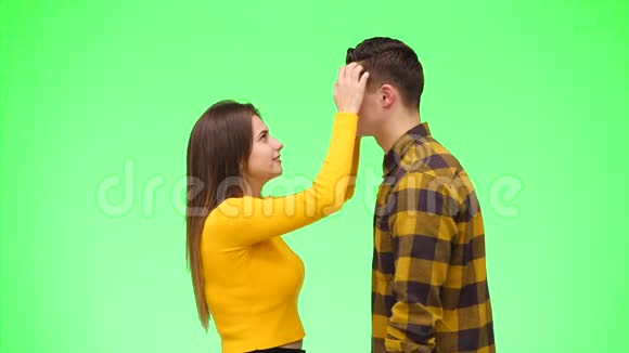 好奇的女孩拍拍她男孩的头发并把他拉近亲吻在一个绿色的背景快关门复制空间4K视频的预览图