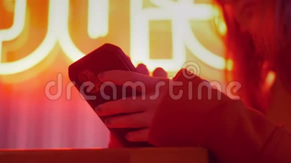 特写女人用手机触摸屏手彩色霓虹灯持有智能手机社会传播视频的预览图