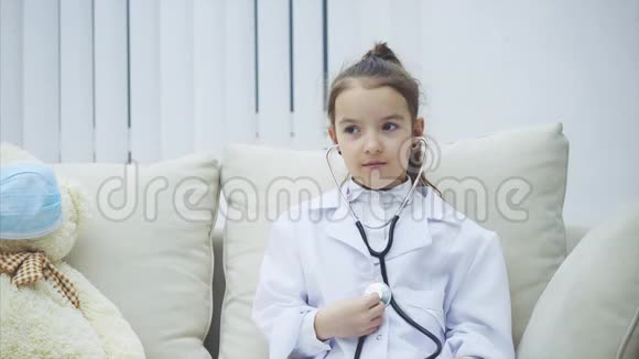 穿着医用外套的小女孩正在检查自己然后用听诊器检查泰迪熊惊讶的表情视频的预览图