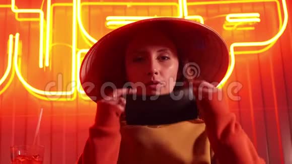 冠状病毒病原体爆发大流行的概念戴着城市防护或医疗面罩的女人看着霓虹灯上的摄像机视频的预览图
