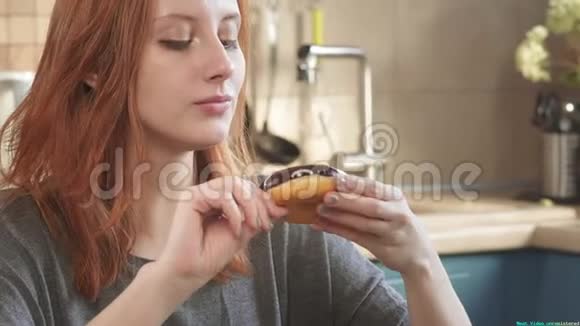 迷人的饥饿红发女孩吃甜甜圈在清晨周末在厨房不健康的饮食脂肪视频的预览图