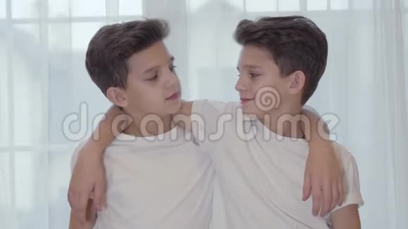 高加索双胞胎看镜头微笑的肖像双胞胎兄弟穿着类似的白色T恤衫手挽手视频的预览图