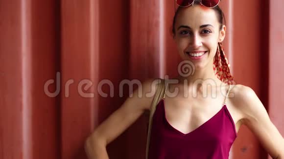 一位身穿勃艮第圣礼的年轻女子在红墙背景上摆姿势看着卡梅拉戴上粉红色眼镜视频的预览图