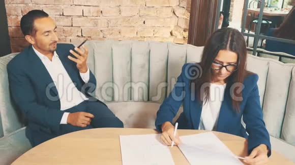 两个商人在一家咖啡馆工作女人正在用心学习文件男人在视频聊天在模糊视频的预览图