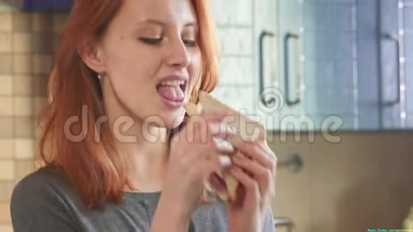 迷人的年轻红发女孩在周末在厨房里吃一个俱乐部三明治吃不饱的女人视频的预览图