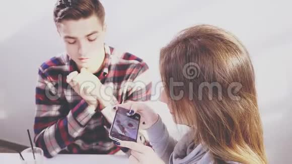可爱的女孩正在为美味的甜点拍照坐在咖啡馆的桌子旁男孩感到无聊和震惊视频的预览图