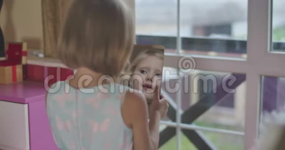 后视年轻的高加索女孩手中拿着镜子微笑孩子的脸在镜子里反射射击视频的预览图