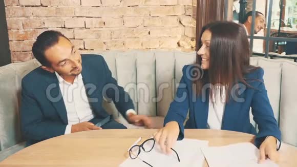 两个商人在一家咖啡馆工作女人戴上眼镜开始签署文件男人鼓励她关闭视频的预览图
