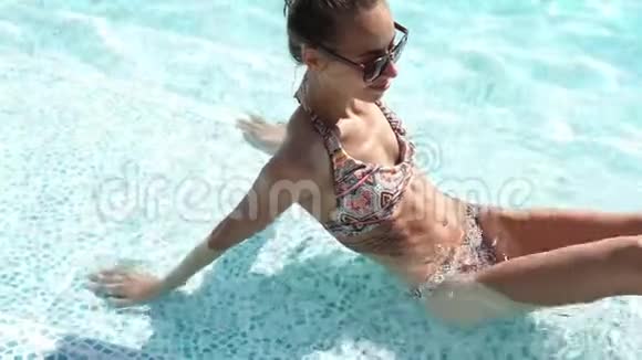 年轻苗条性感的比基尼女郎坐在豪华酒店的游泳池里在水中放松视频的预览图