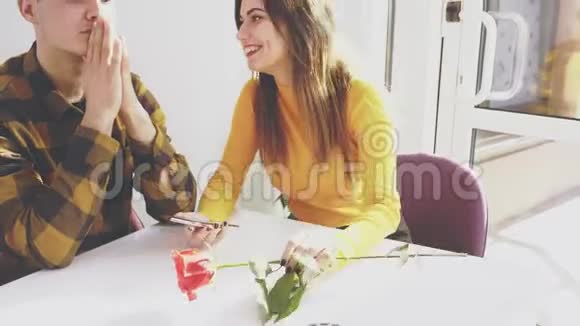 可爱的女孩坐在咖啡馆的桌子旁她正在和她的男朋友交流给他看一些关于视频的预览图