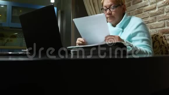 使用笔记本电脑在家拿文件的老年妇女视频的预览图