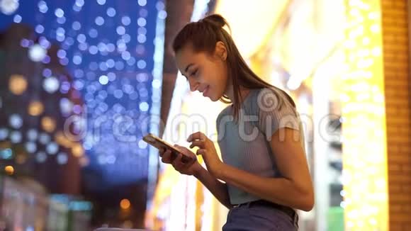 美丽的微笑的年轻女子坐在阳光明媚的城市街道上有许多灯使用手机视频的预览图
