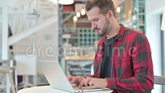 有头痛的年轻人在咖啡厅用笔记本电脑视频的预览图