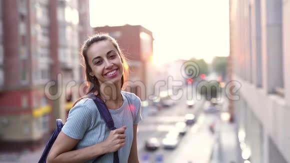 幸福微笑的年轻女子看着相机在夕阳的城市背景上欢快地微笑着视频的预览图