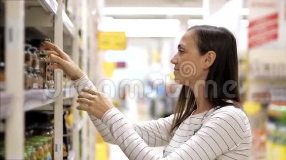 年轻女子在超市的玻璃罐里选择罐装蘑菇视频的预览图