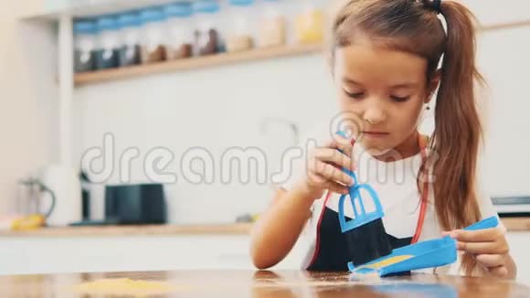 一个穿深色迪基的小漂亮女孩用蓝色的扫把和铲子清洁厨房的桌子失去理智作物4K视频的预览图