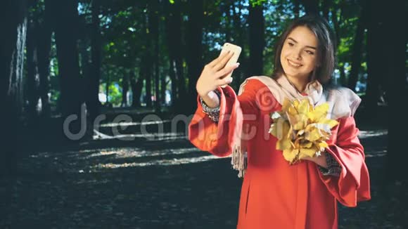 可爱的女孩拿着一束秋叶用手机自拍背景模糊复制空间4K视频的预览图