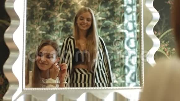 两个留着长发的年轻金发女郎为聚会做准备站在镜子旁微笑视频的预览图
