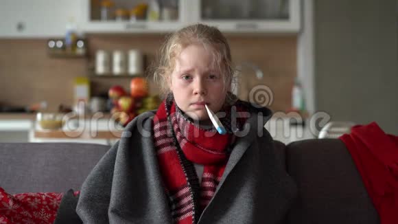 冷白种人女孩在家一个穿着围巾和格子的生病孩子的滑稽肖像沙发上有一个温度计视频的预览图