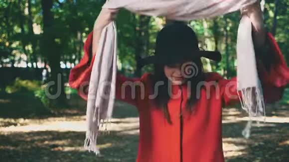 漂亮的年轻女孩带着红色的外套和黑色的帽子轻轻地绑着粉红色的围巾与世隔绝在公园模糊的背景上关闭视频的预览图