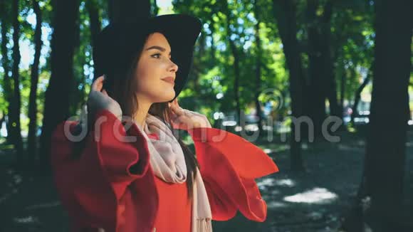 漂亮的年轻女孩带着红色的外套和帽子在公园里看着周围与世隔绝背景模糊快关门复制空间视频的预览图