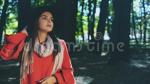 漂亮的年轻女孩带着红色的外套和帽子在公园里看着周围与世隔绝背景模糊复制空间4K视频的预览图