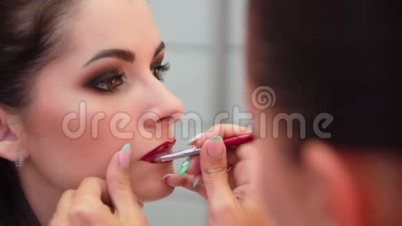 化妆师描绘了年轻女孩的嘴唇用刷子涂你的嘴唇红色化妆师化妆视频的预览图