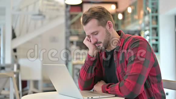 有笔记本电脑的疲惫的年轻人在咖啡馆里打盹视频的预览图