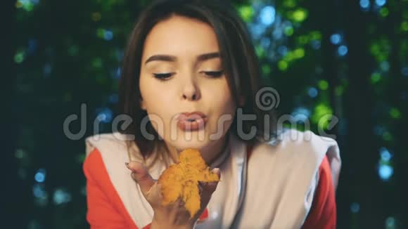 慢点漂亮的年轻女孩穿着一件红色的外套吹着一片黄色的秋叶与世隔绝背景模糊关闭视频的预览图