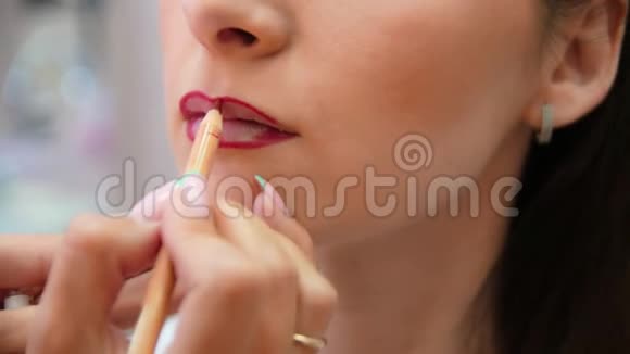 化妆师描绘了年轻女孩的嘴唇用红色铅笔圈出唇边化妆师化妆视频的预览图