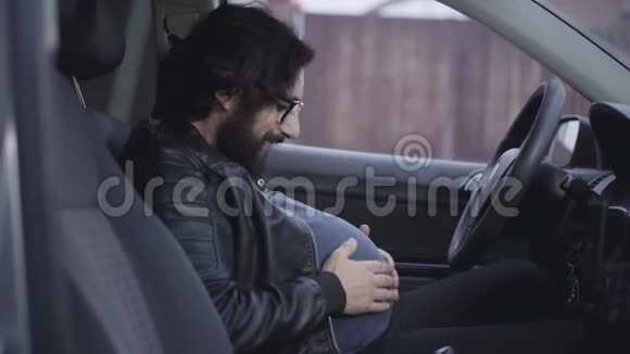 侧视特写滑稽孕妇坐在司机座位上抚摸他的腹部微笑的成年人肖像视频的预览图