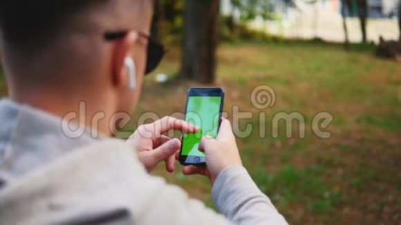 自信和放松的家伙穿着休闲服他正在绿色手机屏幕上选择酷酷的音乐坐在外面视频的预览图