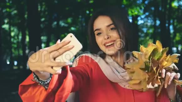 可爱的女孩拿着一束秋叶用手机自拍背景模糊快关门副本视频的预览图