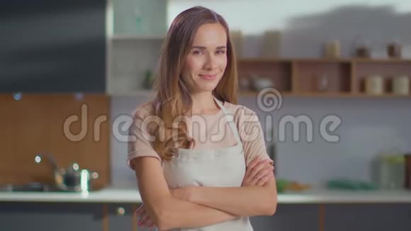 双手交叉的女人站在厨房里家里穿着炊具围裙的女人视频的预览图