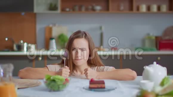 女人在厨房里选择沙拉而不是蛋糕带叉子的女孩尝试新鲜沙拉视频的预览图