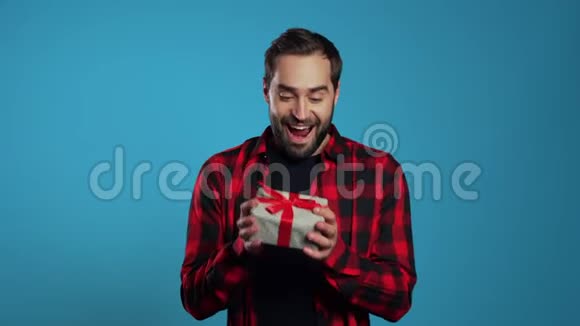 年轻的帅哥微笑着拿着礼品盒在蓝色的工作室背景上有胡子的人视频的预览图