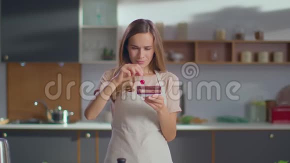女人在厨房用樱桃装饰蛋糕在厨房看摄像机的女人视频的预览图