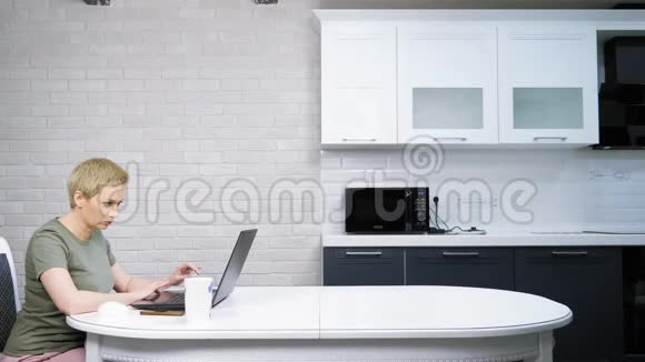 一个女人用笔记本电脑坐在厨房的桌子上视频的预览图