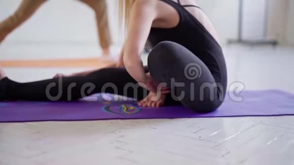 穿着黑色运动服的迷人柔韧女性在瑜伽室锻炼在垫子上伸展背部和腿部视频的预览图