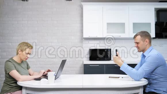 现代的家庭主妇和商人坐在厨房里互相忽视视频的预览图
