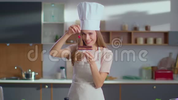糖果师在厨房把樱桃放在蛋糕上女人对着镜头微笑视频的预览图