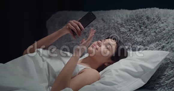 女人在卧室里滚动智能手机视频的预览图